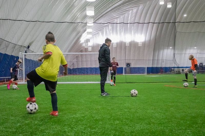 Four kids and coach doing soccer drills in a soccer dome